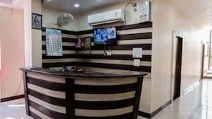 A reception area with a striped counter, air conditioning units, a television, and a wall-mounted clock. - Hotel Swarat (Satna)