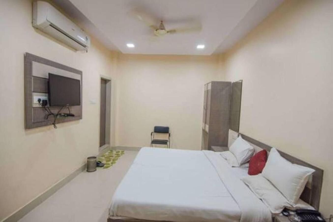 A hotel room with a bed, a chair, an air conditioning unit, a television, and a telephone.