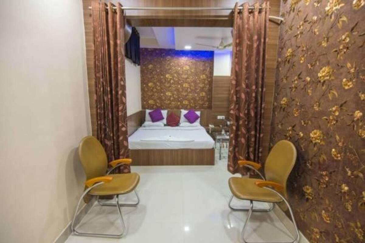 Une chambre d’hôtel avec un lit, deux chaises, un miroir et un mur décoré d’un motif.