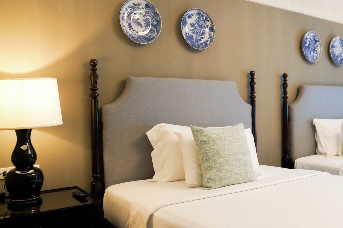 Habitación de hotel con dos camas, cabecero, lámparas de noche y placas decorativas en la pared.