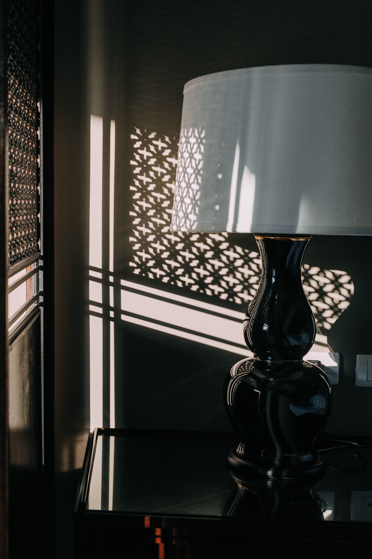 A lamp on a table with a patterned window shade casting shadows.