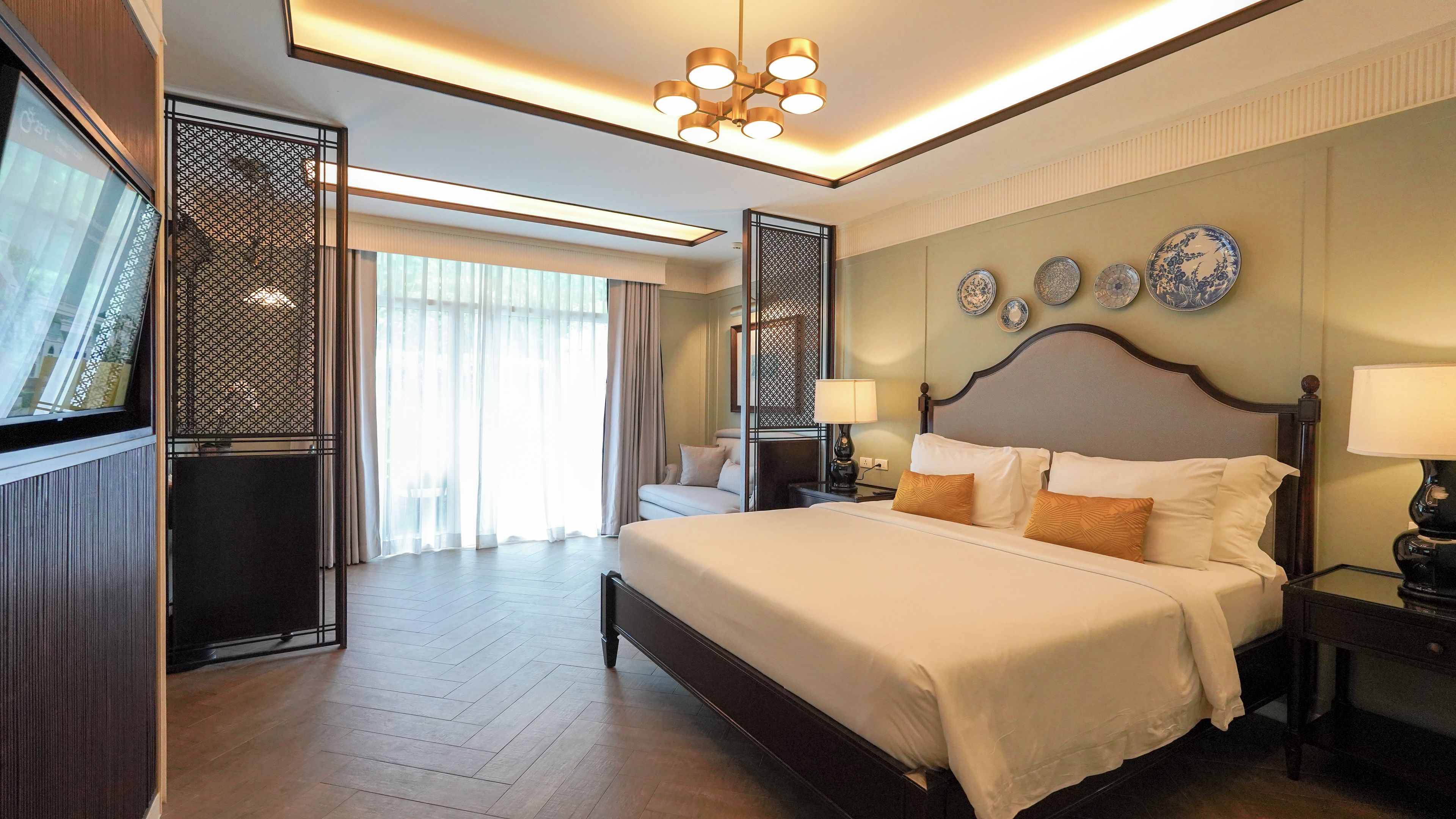 A hotel room with a large bed, bedside tables, a ceiling light fixture, and decorative plates on the wall.