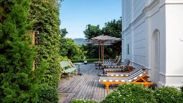 Una terraza de madera con mobiliario exterior, un espacio de estar cubierto y abundante vegetación.