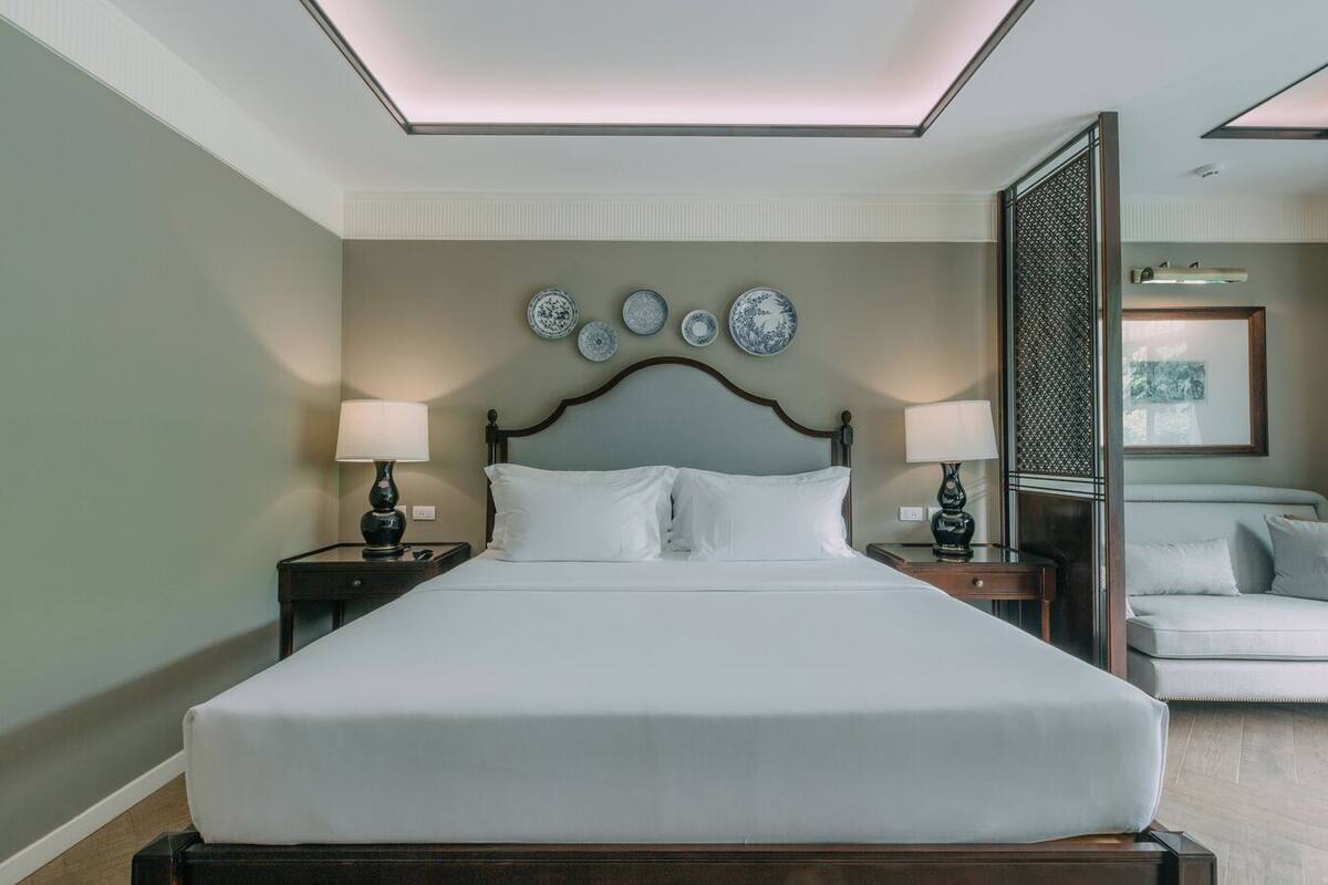 Habitación de hotel con una cama grande, dos mesitas de noche, un sofá y una pared decorativa con platos.