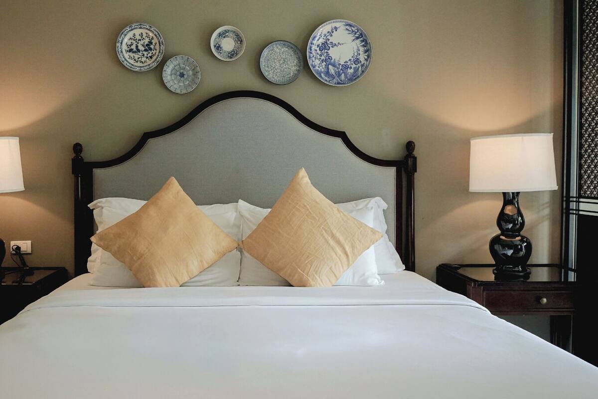 Una cama bien hecha con dos almohadas, un cabecero, mesitas de noche con lámparas y platos decorativos en la pared.