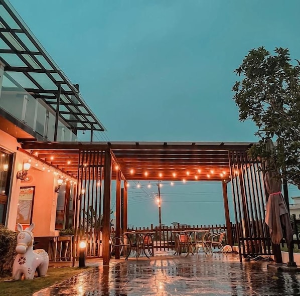 A covered outdoor seating area with string lights, a pergola, and a dining table with chairs. - Marburg Hall (Sanxing)