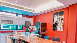 A modern kitchen with a central island, a dining area with a wooden table and chairs, and a red accent wall with a horse painting. - Marburg Hall (Sanxing)