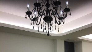 A modern living room with a flat-screen TV mounted on the wall, a wooden chest of drawers with the word "HOME" on it, a white refrigerator, and a black chandelier. - Marburg Hall (Sanxing)