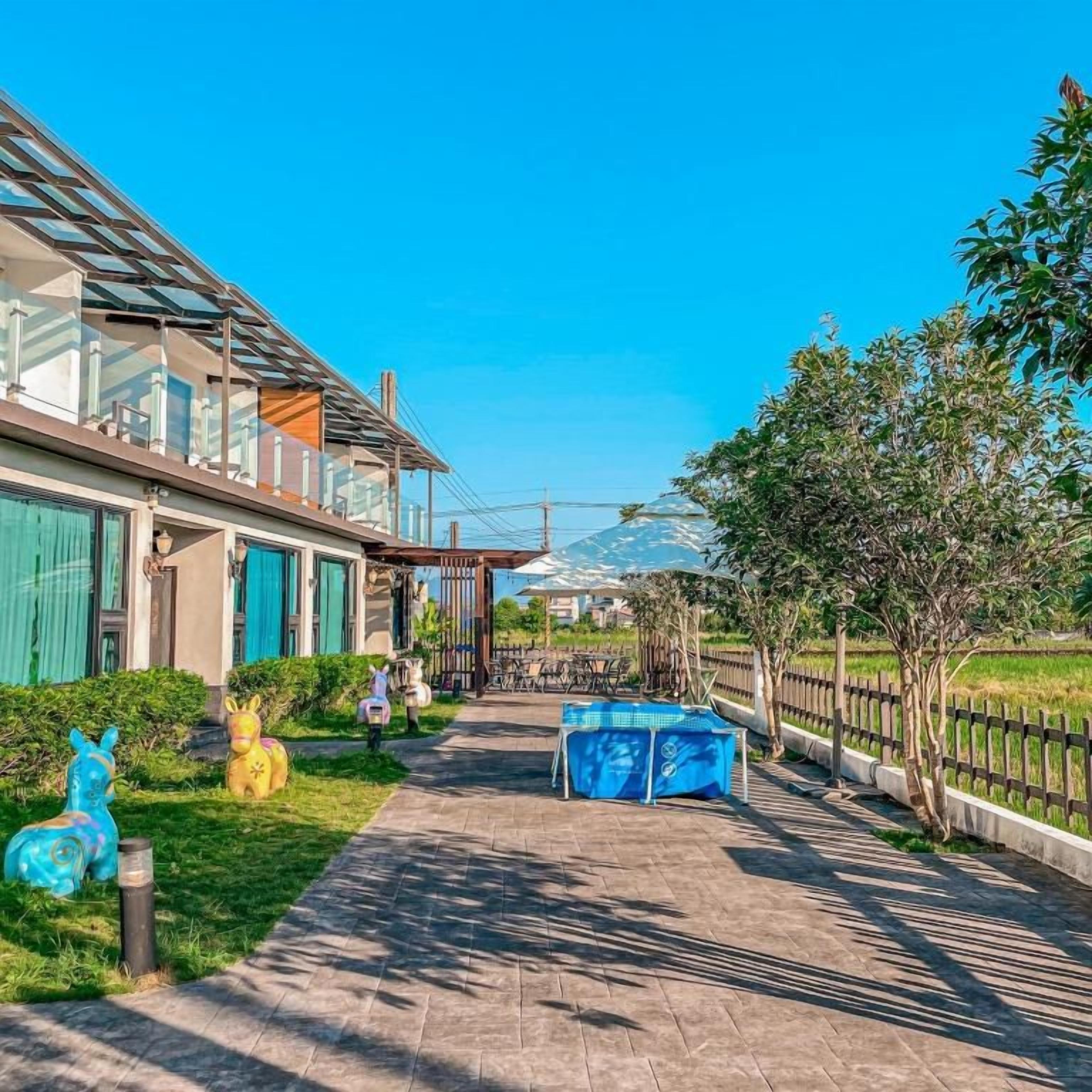 A pathway leading to a building with a glass roof, surrounded by greenery and a fenced area.