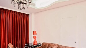 A living room with a brown leather sofa, a red curtain, a black lamp, a chair, and two blue suitcases. - Marburg Hall (Sanxing)