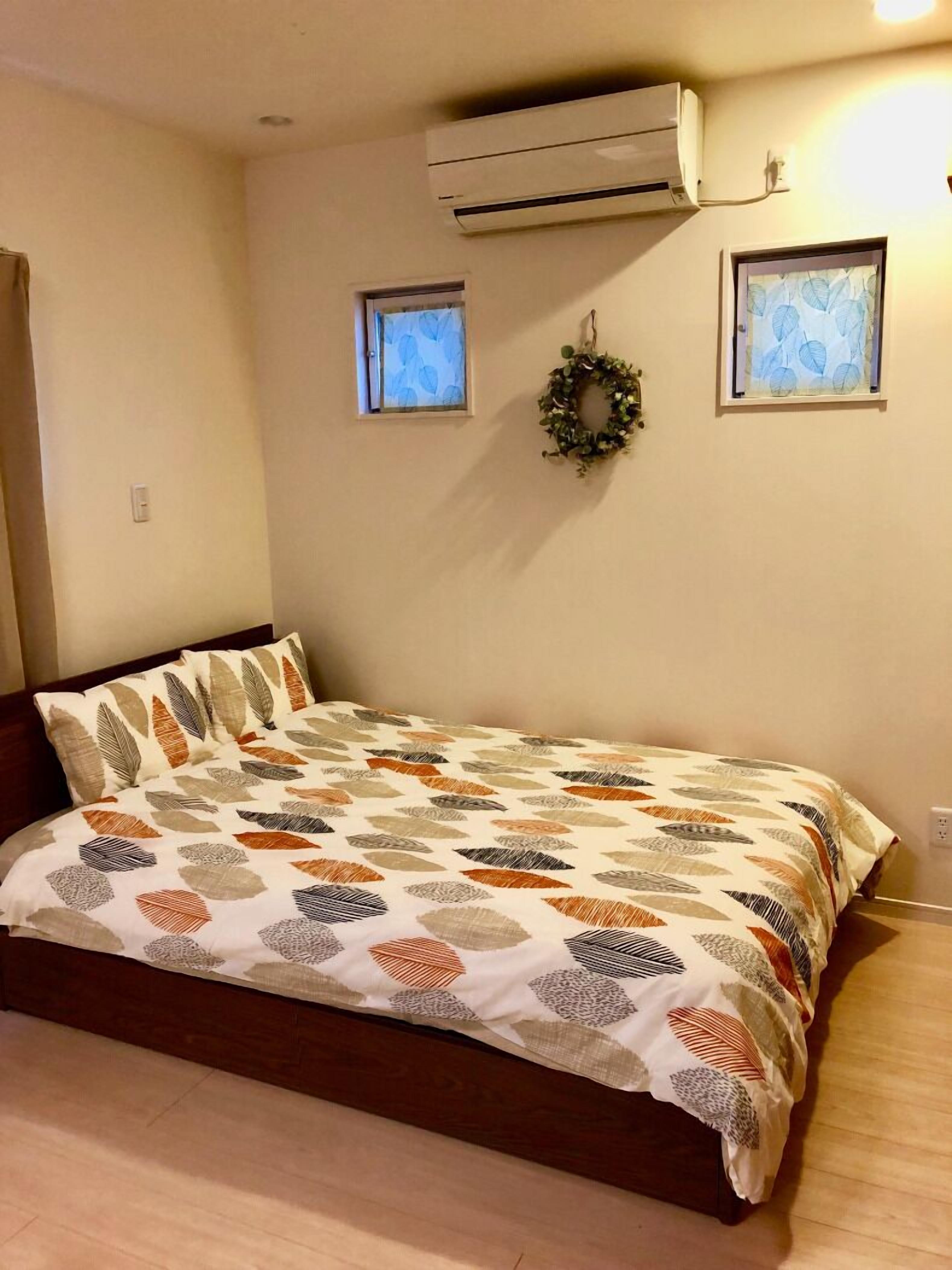 Ein Schlafzimmer mit einem Bett, einer Klimaanlage, zwei kleinen Fenstern und einem an der Wand befestigten Kranz.