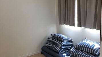 A room with a wooden floor, a window with grey curtains, and a stack of striped pillows.
