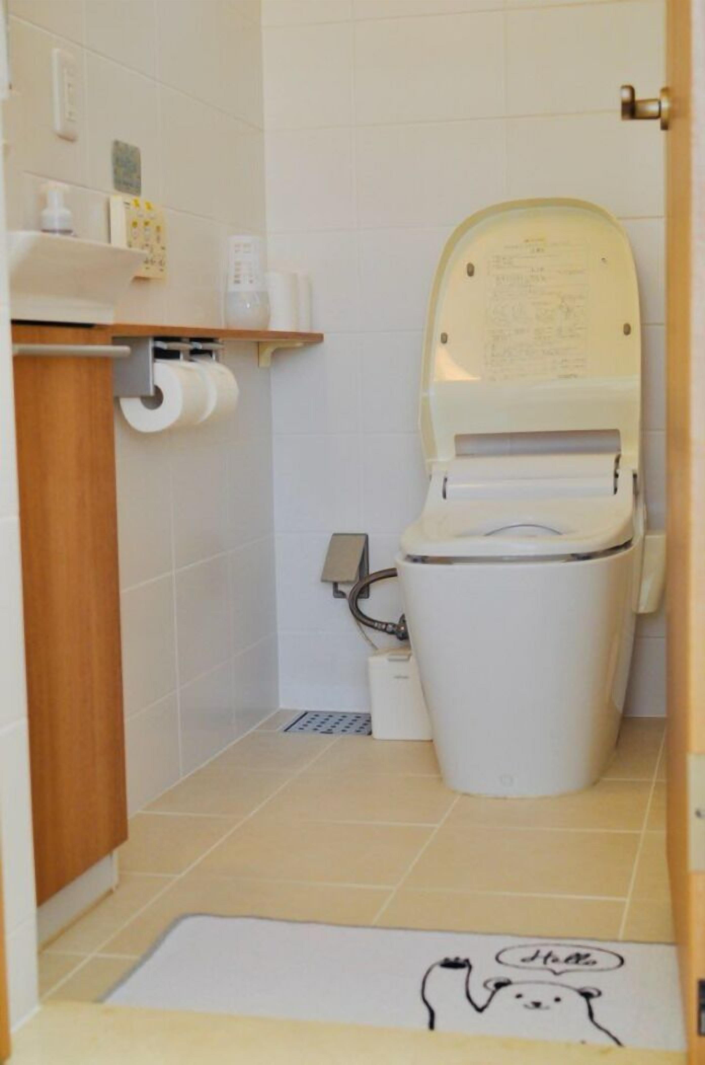 A small bathroom with a toilet, a shelf with toiletries, and a floor mat with a bear design.