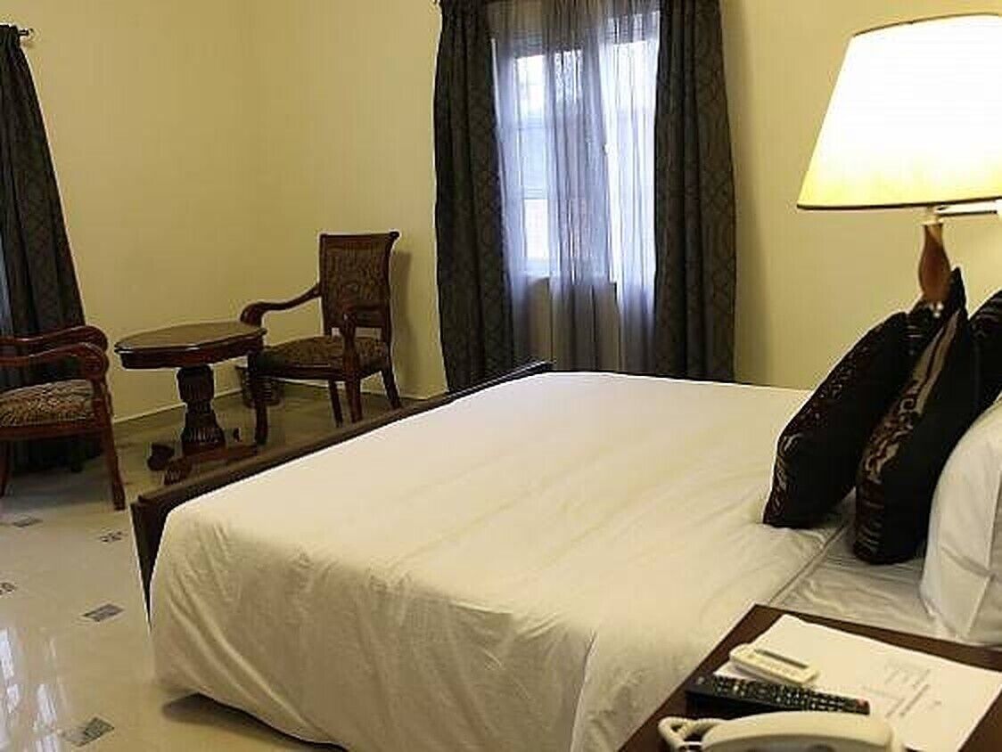 A hotel room with a large bed, a bedside table with a lamp, a chair, and a small table.