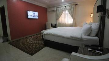 A hotel room with a bed, a television mounted on the wall, a desk with a chair, and a window with curtains.