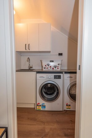 A laundry room with two Bosch washing machines, a sink, and white cabinets. - Tree Walk - Redwoods, Spa Pool, Sleeps 10 (Rotorua)