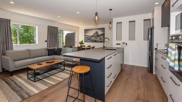 Eine moderne Küche mit einer zentralen Kochinsel, einem Essbereich mit Sofa und Couchtisch sowie großen Fenstern mit Vorhängen.