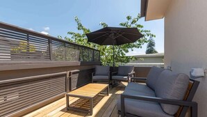 Eine Terrass mit Holzboden, einer Couch, zwei Stühlen und einem großen Sonnenschirm.