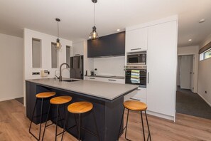 A modern kitchen with a central island, bar stools, and built-in appliances. - Tree Walk - Redwoods, Spa Pool, Sleeps 10 (Rotorua)