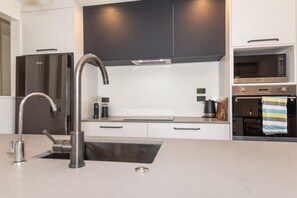 A modern kitchen with stainless steel appliances, a built-in oven, and a sleek faucet. - Tree Walk - Redwoods, Spa Pool, Sleeps 10 (Rotorua)