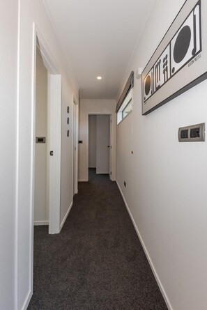 A hallway with carpeted flooring, white walls, and a door on the left. - Tree Walk - Redwoods, Spa Pool, Sleeps 10 (Rotorua)