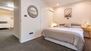 Ein Schlafzimmer mit einem Bett, Nachttischlampen, einem an der Wand befestigten Spiegel und einem gerahmten Bild.