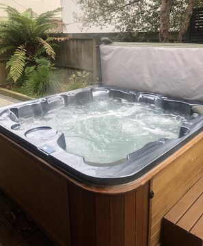 A hot tub with a wooden exterior, surrounded by a wooden deck and a metal fence. - Tree Walk - Redwoods, Spa Pool, Sleeps 10 (Rotorua)