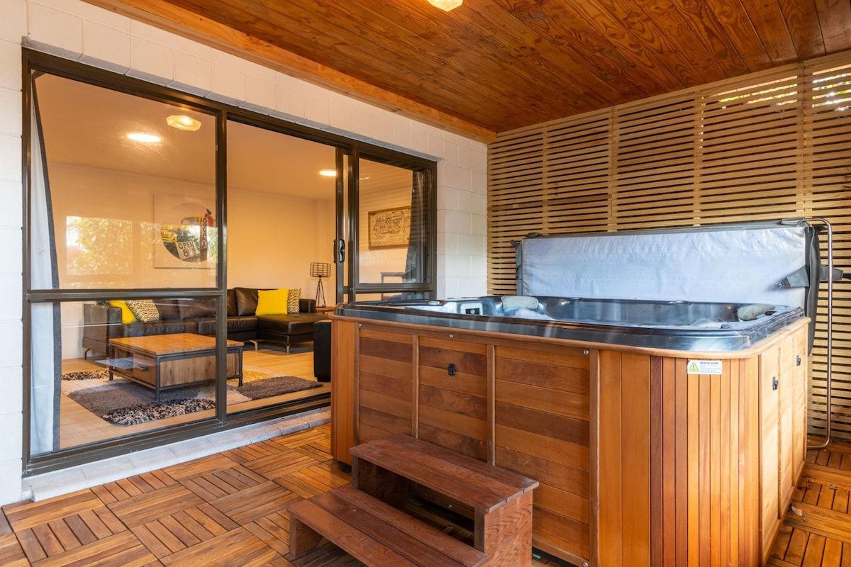A wooden hot tub with a bench in front, a sliding glass door leading to a living area, and a wooden ceiling.