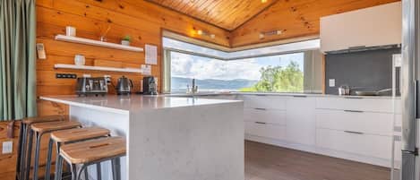 A modern kitchen with a central island, wooden ceiling, and a view of the outdoors.