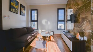 A modern living room with a sofa, a round coffee table, and a TV on a wall. - Yen Vang Hotel & Apartment (Nha Trang)