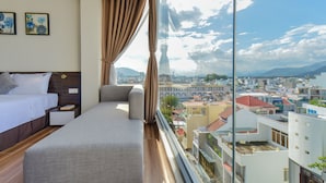 A hotel room with a bed, a chair, a nightstand, and a large window offering a city view. - Yen Vang Hotel & Apartment (Nha Trang)