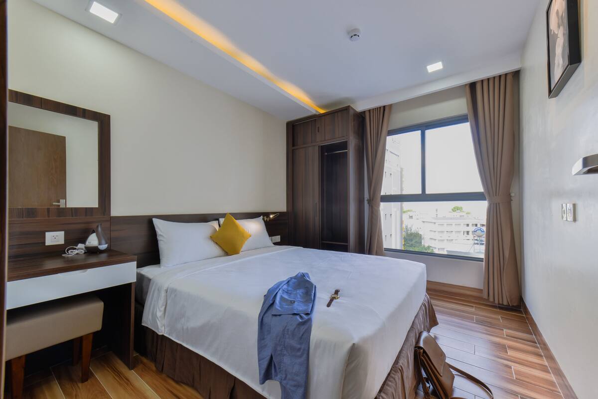 A hotel room with a bed, bedside table, and a window with curtains.