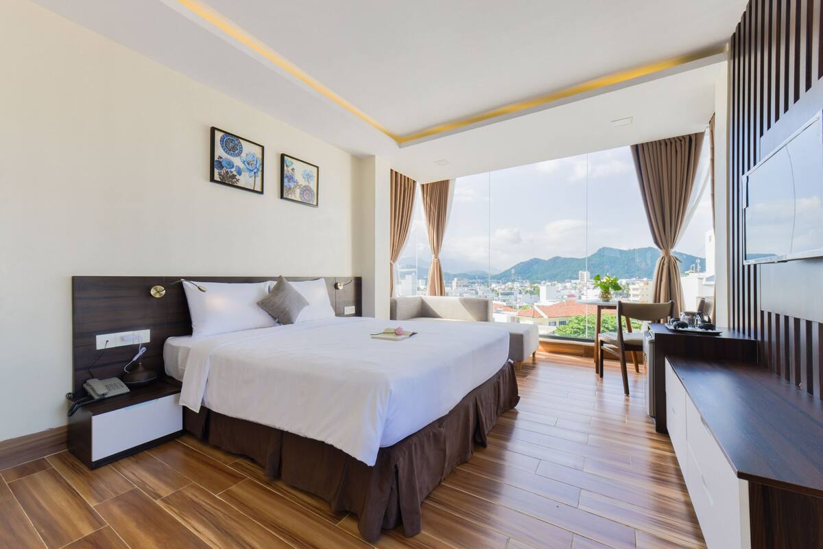 A hotel room with a large bed, a desk, and a view of the city.