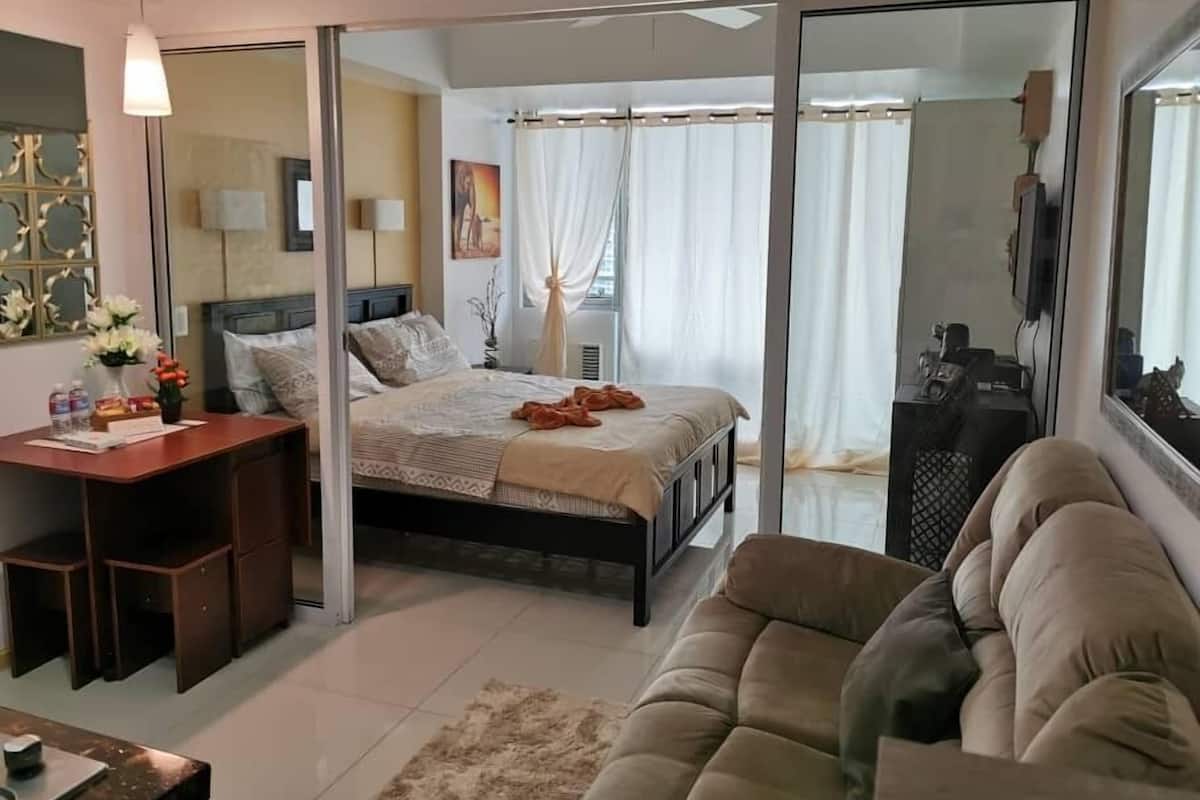 A bedroom with a bed, a desk, a sofa, and a sliding glass door leading to a bathroom.