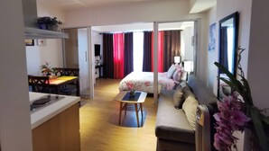 Een moderne hotelkamer met kitchenette, eethoek, bank en een bed met gordijnen.