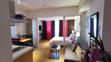 A modern hotel room with a kitchenette, a dining area, a sofa, and a bed with curtains.