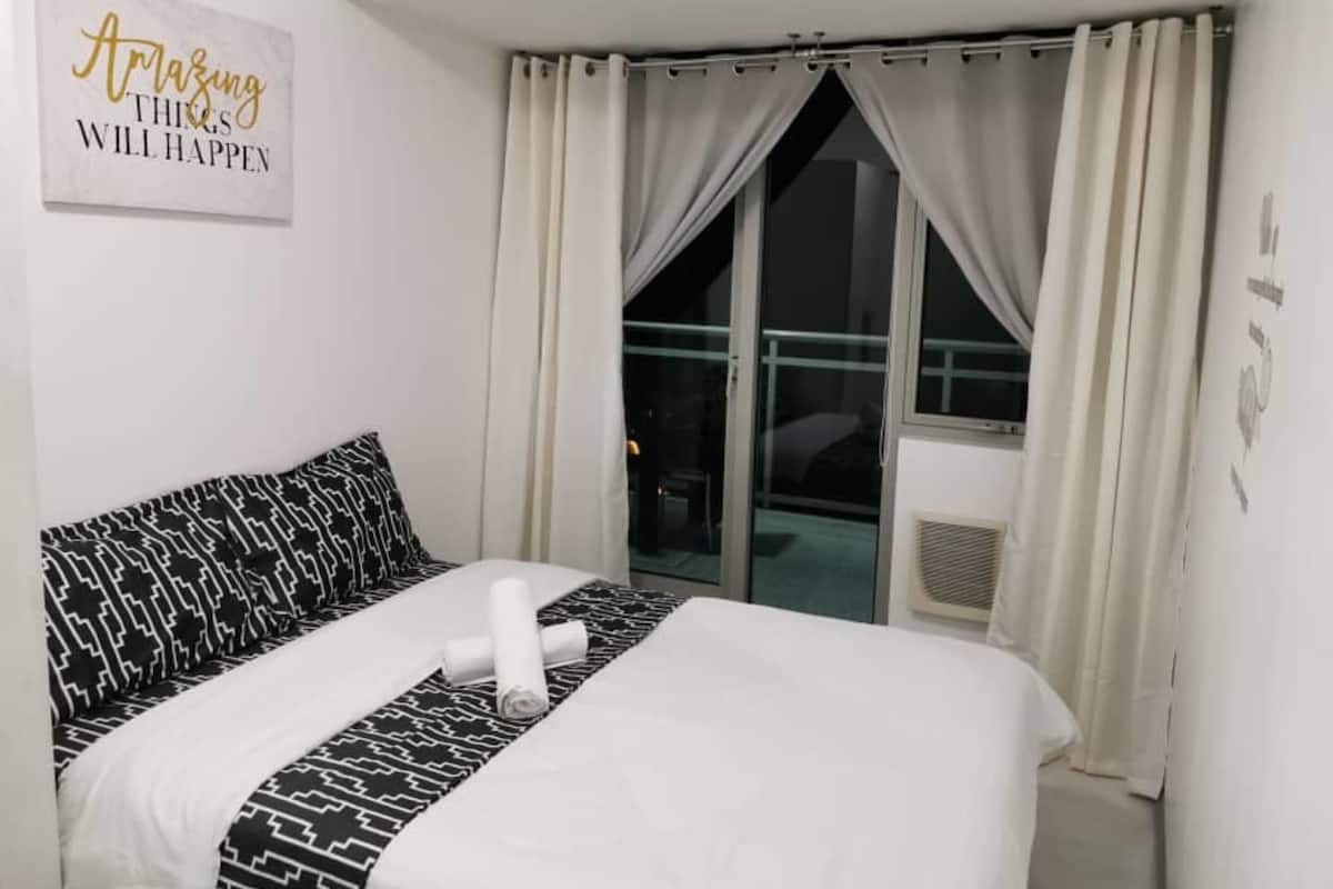 A hotel room with a bed, a window with curtains, a wall with a motivational quote, and a view of the outside.