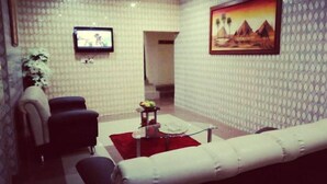 A living room with a white patterned wall, a white sofa, a red rug, and a television on the wall. - Global Dreams Hotel (Calabar)
