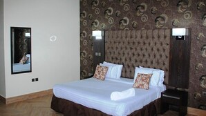 A neatly made bed with a brown skirt, a tufted headboard, and two bedside lamps. - Global Dreams Hotel (Calabar)