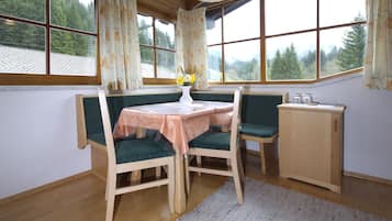 A cozy room with a wooden table and chairs, a small cabinet, and a view of a forest through large windows.