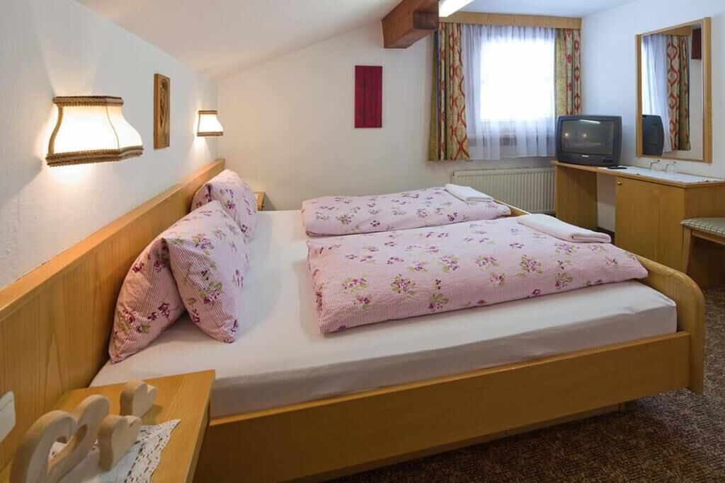Une chambre avec un lit simple, un bureau avec une tél évision et une fenêtre avec des rideaux.
