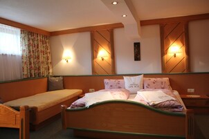 Habitación de hotel con una cama individual, un sofá pequeño, dos lámparas fijadas a la pared y una ventana con cortinas estampadas.