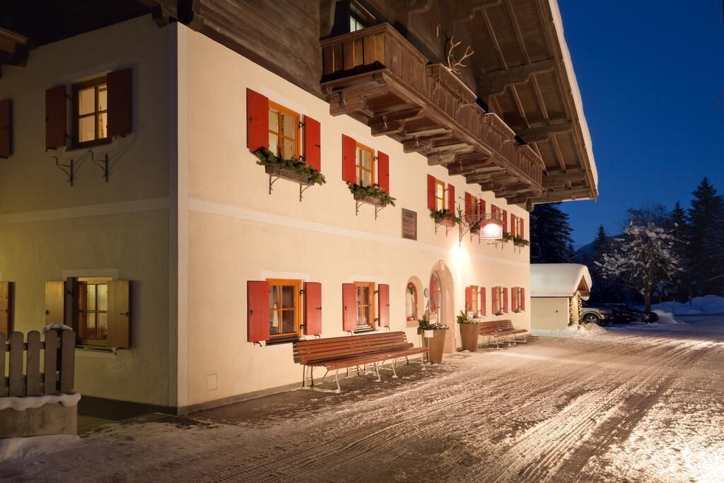A multi-story building with red shutters, a wooden balcony, and a snow-covered ground.