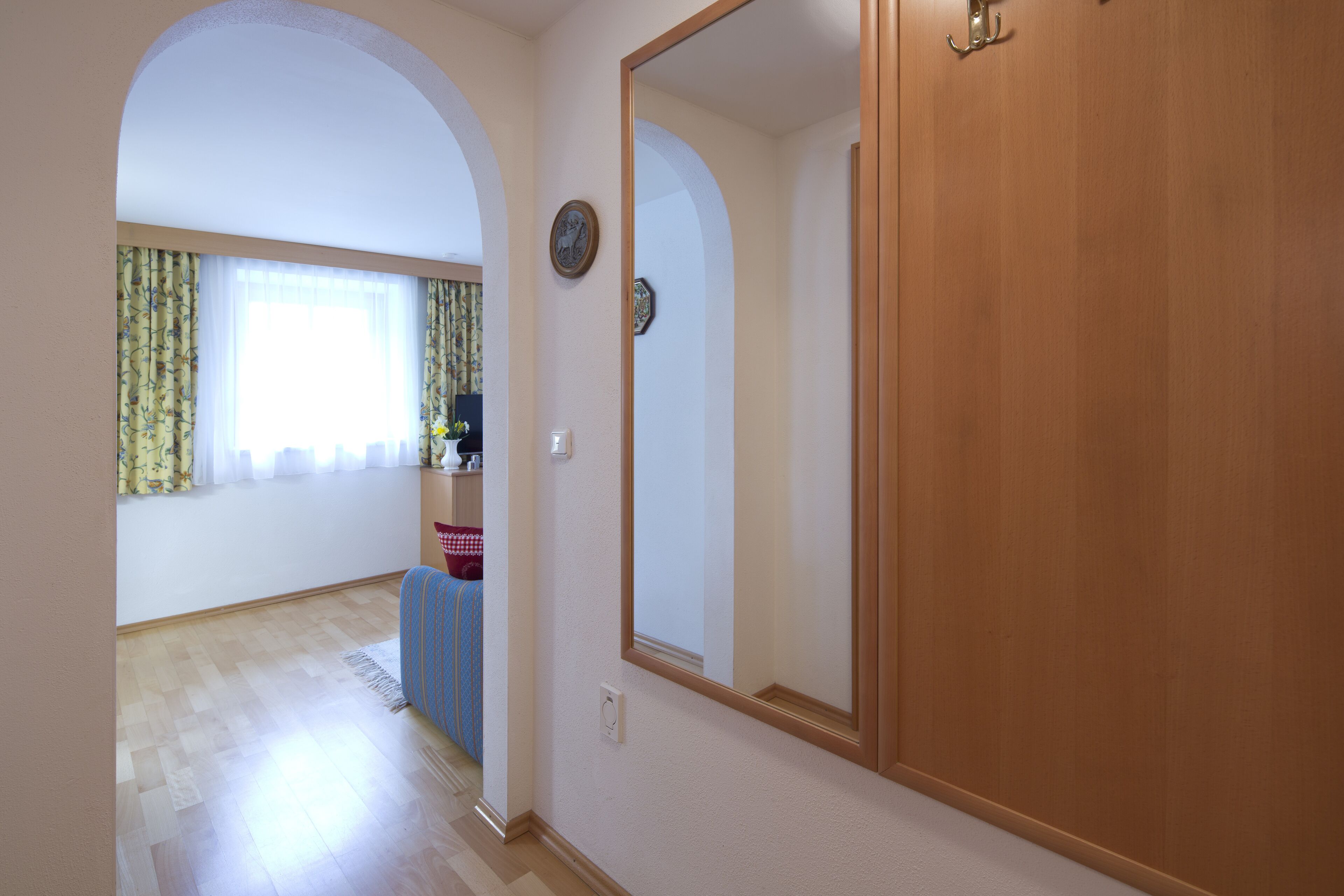 Une pièce avec une porte en bois, un grand miroir et une fenêtre avec des rideaux.