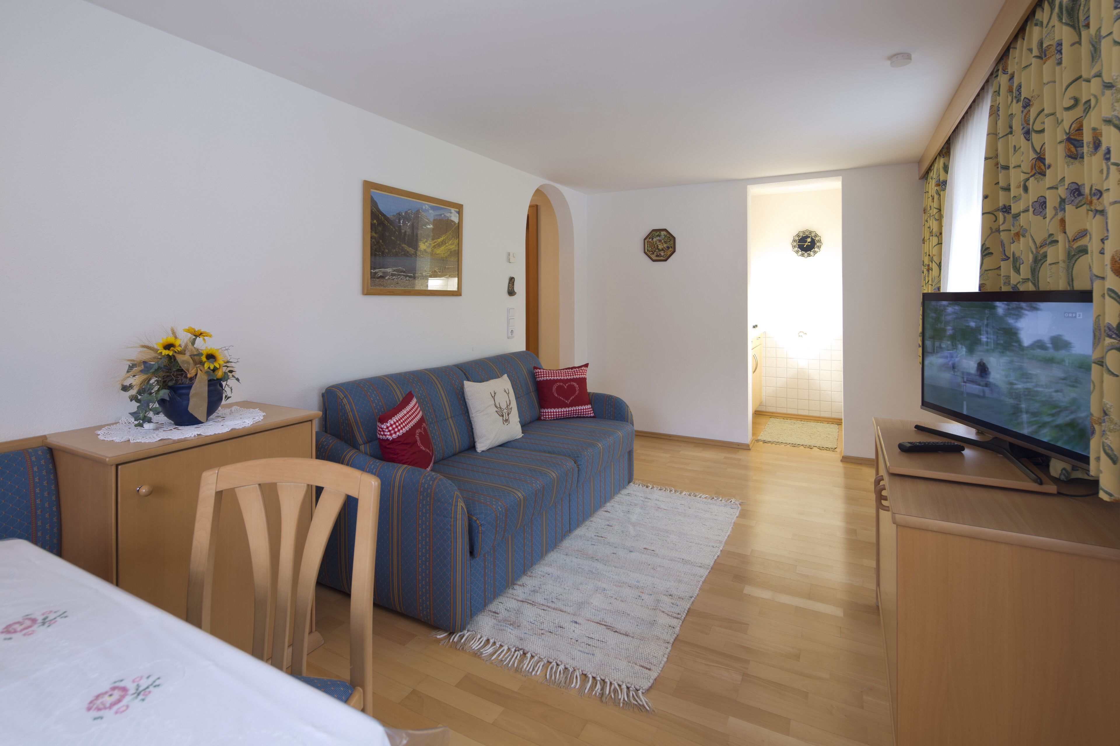 A cozy living room with a sofa, a TV, and a small table with a vase of flowers.
