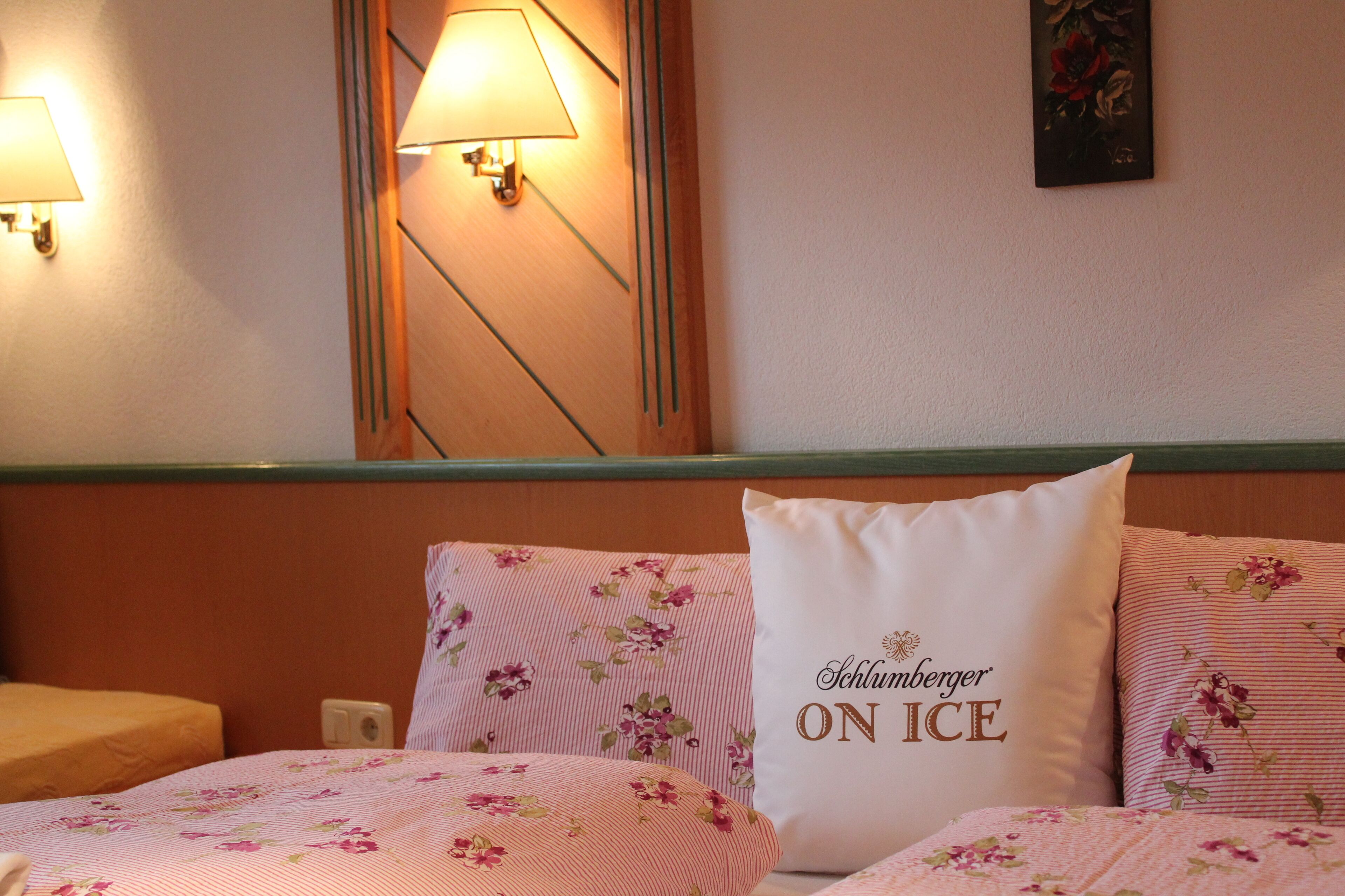 Ein Hotelzimmer mit floralem Bettbezug, einem Bett mit einem Kopfkissen mit der Aufschrift "Schlumberger ON ICE" und Wandlampen.