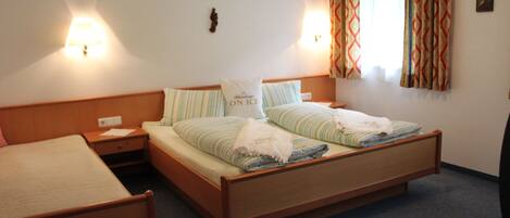 A hotel room with two single beds, a nightstand, a lamp, a window with curtains, and a wall-mounted decoration.