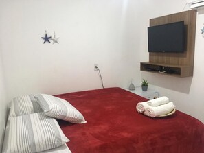 A bedroom with a red bedspread, striped pillows, a mounted TV, and a small plant on a nightstand.