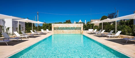 A rectangular swimming pool with clear blue water, surrounded by white lounge chairs and umbrellas.