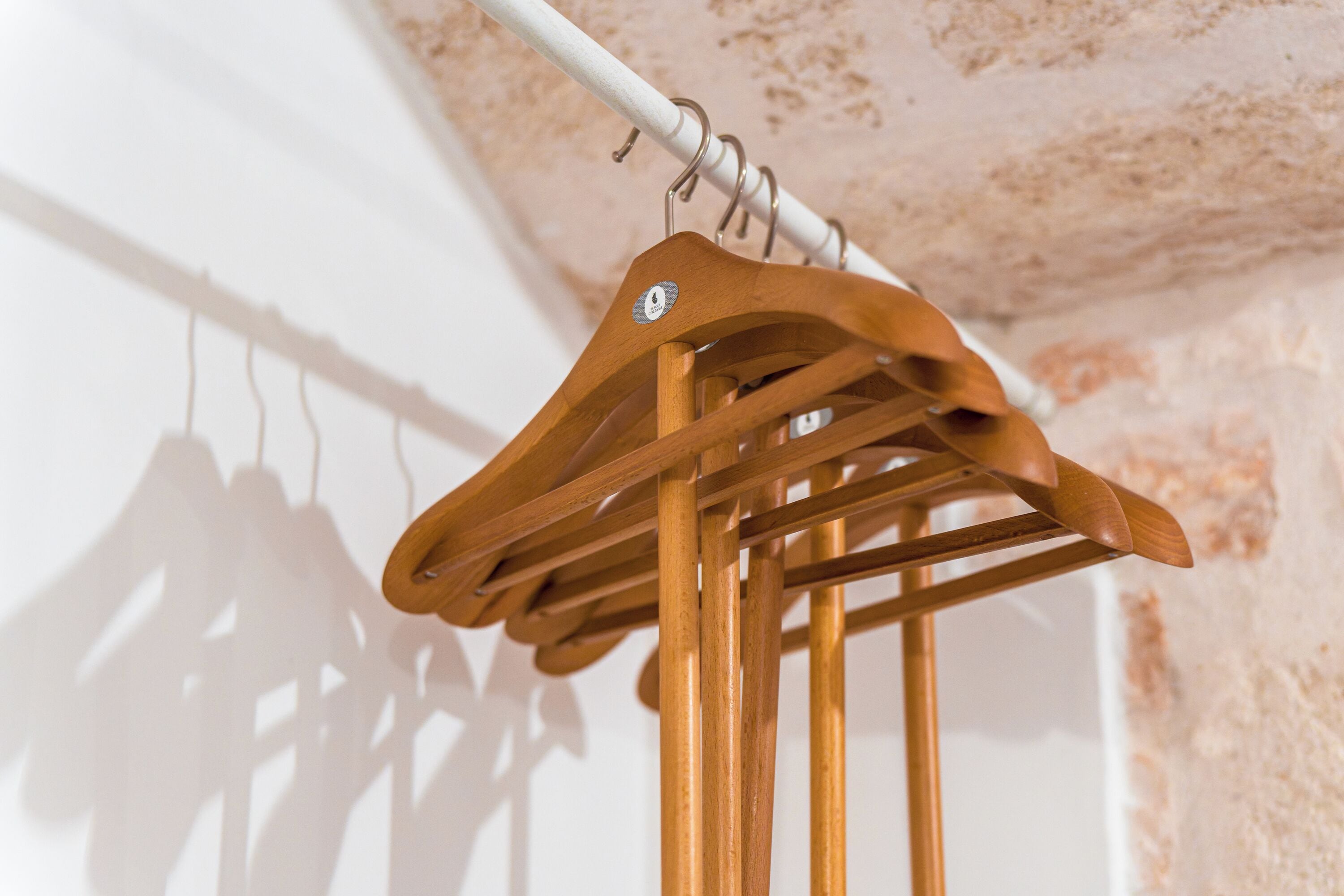 Ein Kleiderständer aus Holz mit mehreren Kleiderbügeln vor einer strukturierten Wand.